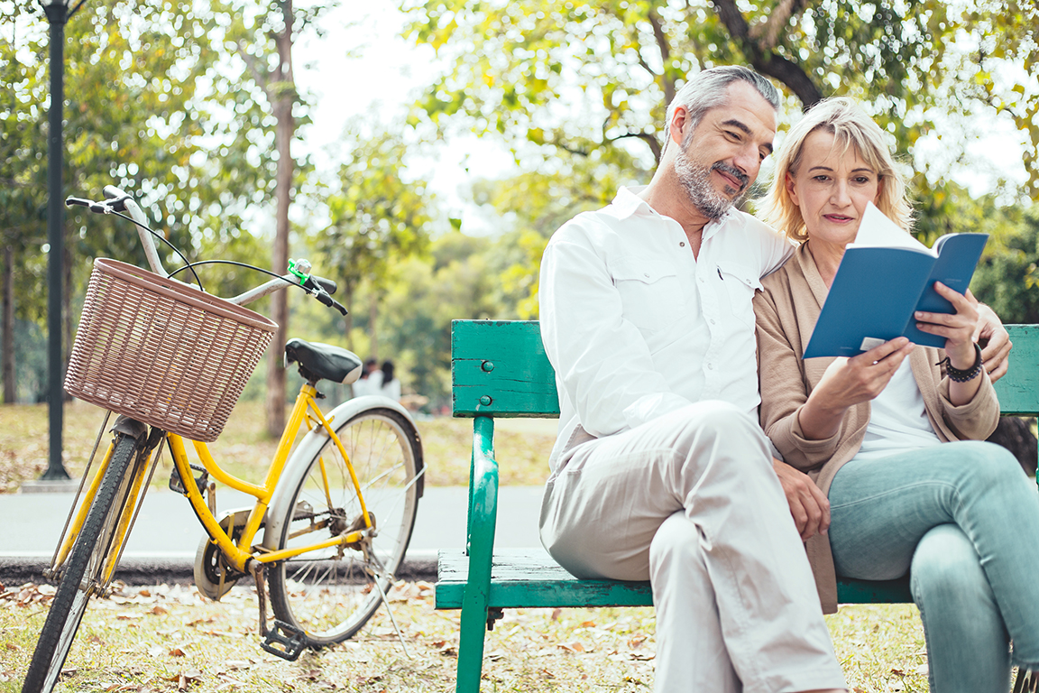 a man and woman sitting on a bench reading a book